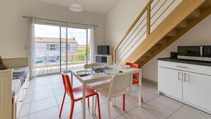 A modern kitchen with white cabinets, a dining area with red chairs, and a wooden staircase. - Appartement Proche Plage (La Rochelle)