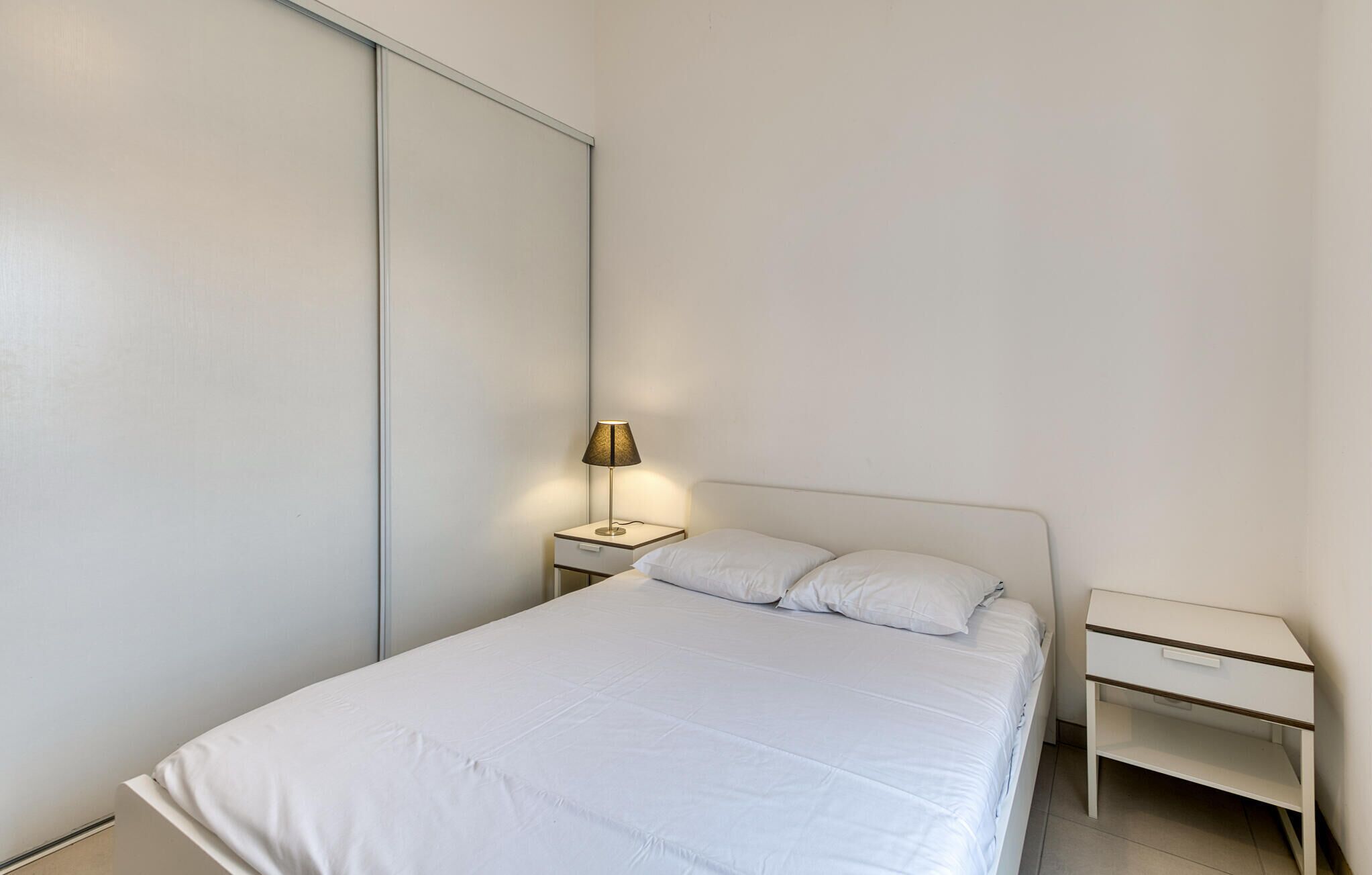 A minimalist bedroom with a bed, a bedside lamp, and a nightstand.