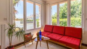 A bright living room with a red sofa, a small wooden table, and a potted plant.