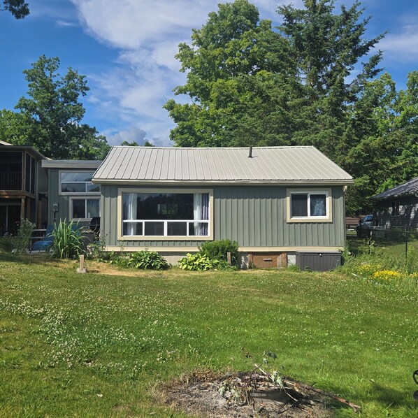 A single-story house with a metal roof, a front porch, and a small garden area. - Charming 3-bedroom cottage in serene Trent Hills with WiFi (Trent Hills)