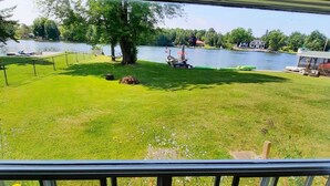 A view from a balcony overlooking a grassy area with a lake, a boat, and a small dock. - Charming 3-bedroom cottage in serene Trent Hills with WiFi (Trent Hills)