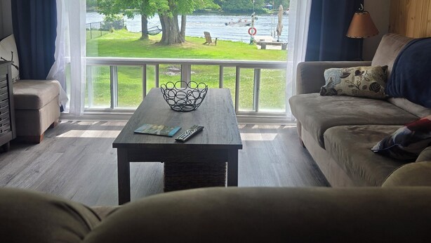 A living room with a view of a lake, a sofa, a coffee table, and a lamp. - Charming 3-bedroom cottage in serene Trent Hills with WiFi (Trent Hills)
