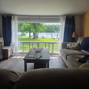 A living room with a view of a lake, a sofa, a coffee table, and a lamp. - Charming 3-bedroom cottage in serene Trent Hills with WiFi (Trent Hills)