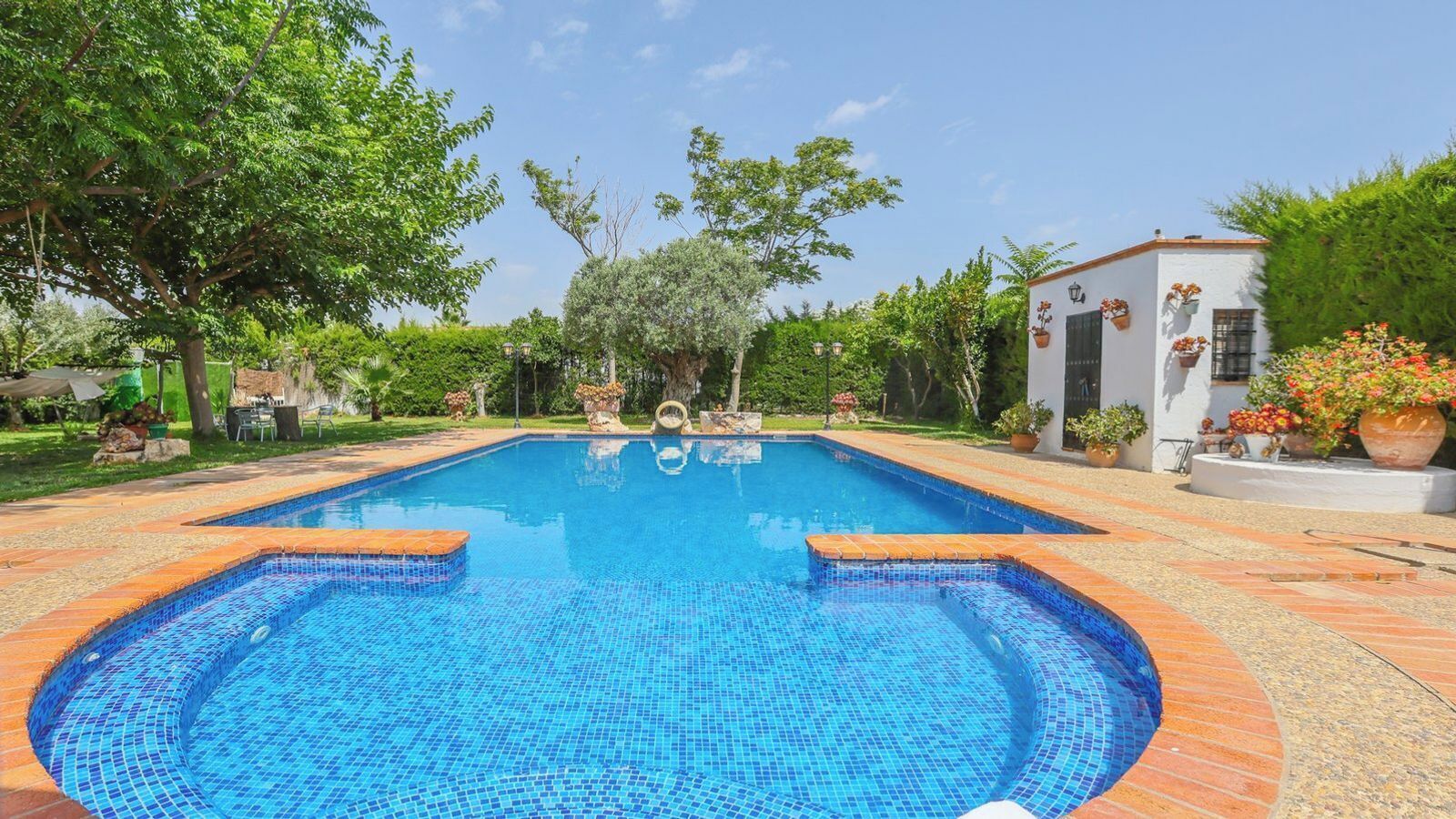 Ein rechteckiger Pool mit blauen Mosaikfliesen, umgeben von einer Ziegelterrasse.