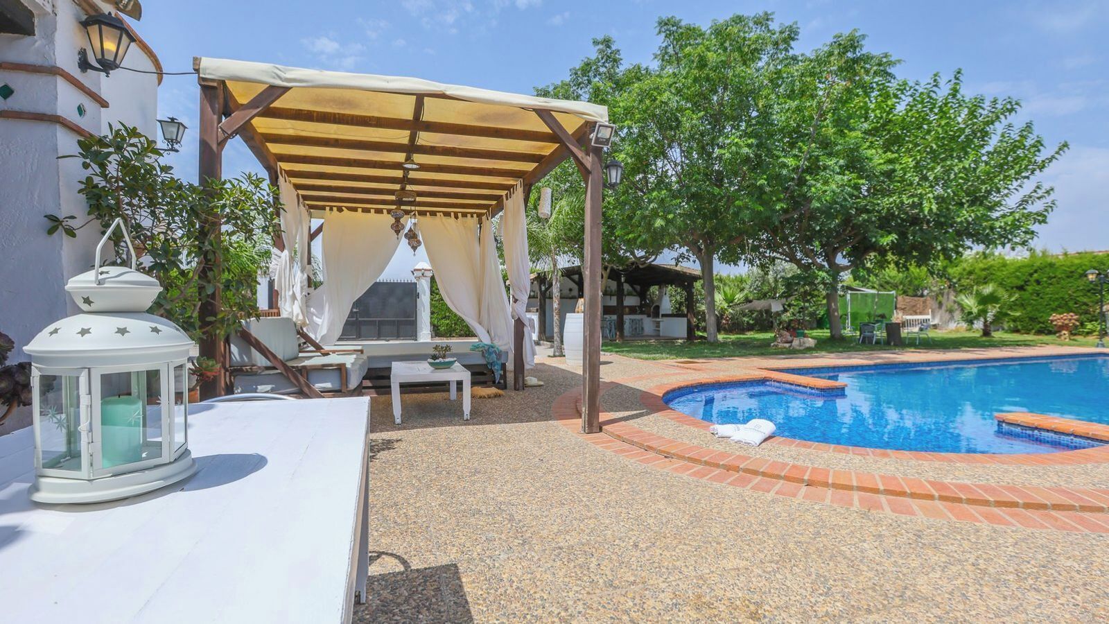 A pool area with a pergola, lounge chairs, and a lantern.