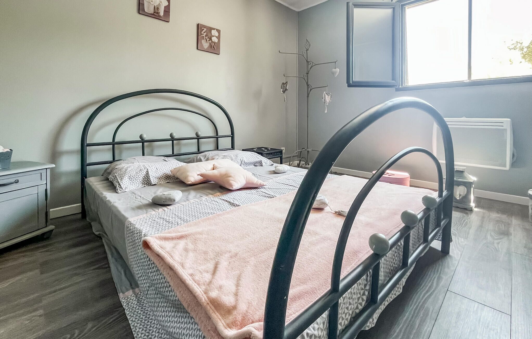 Un lit bien fait, recouvert d’une couverture rose, une table de chevet avec une lampe et une fenêtre donnant sur l’extérieur.