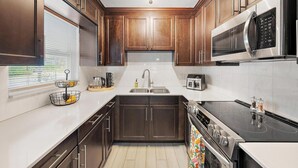 Una cocina moderna con armarios de madera oscura, electrodomésticos de acero inoxidable y una isla central con pileta y hervidor.