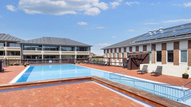 Een zwembad op het dak met een helderblauwe lucht, een terras van baksteen en ligbedden.