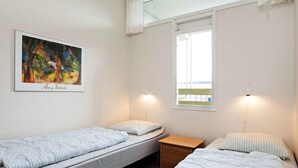 Een kamer met twee eenpersoonsbedden, een klein houten nachtkastje, een lijst met een schilderij en een raam met uitzicht.