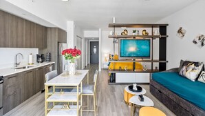 A modern kitchen with a dining area, a living room with a sofa and TV, and a hallway leading to a door. - New Penthouse Downtown Heated pool & jacuzzi (Miami)