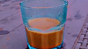 Un verre de café glacé sur une table en bois, avec un paysage montagneux en arrière-plan.