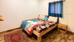 Une chambre à coucher avec un lit en bois, un tapis rouge à motifs, un ventilateur de plafond et une fenêtre avec des rideaux bleus.