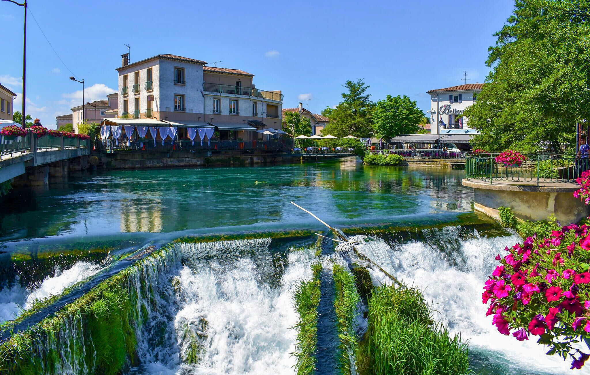 Un río con cascada, un puente y edificios con terrazas.