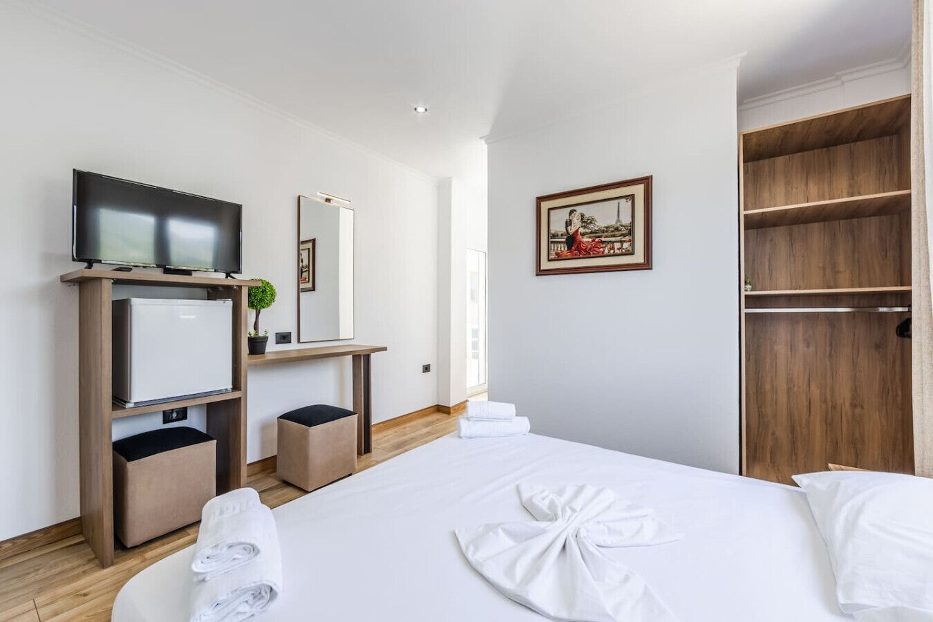 Hotelkamer met een bed, een televisie, een bureau met spiegel, een kledingkast en een lijst aan de muur.