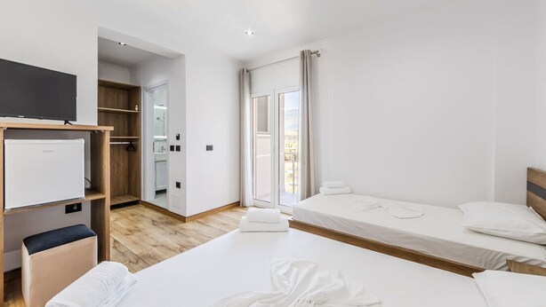 Une chambre d’hôtel moderne avec deux lits, une télévision, une armoire et une salle de bain visible à travers une porte ouverte.