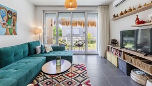A modern living room with a teal sofa, a coffee table, and a TV on a wooden shelf. - Talea Joyful Stay by PikHost by PikHost (Tale)