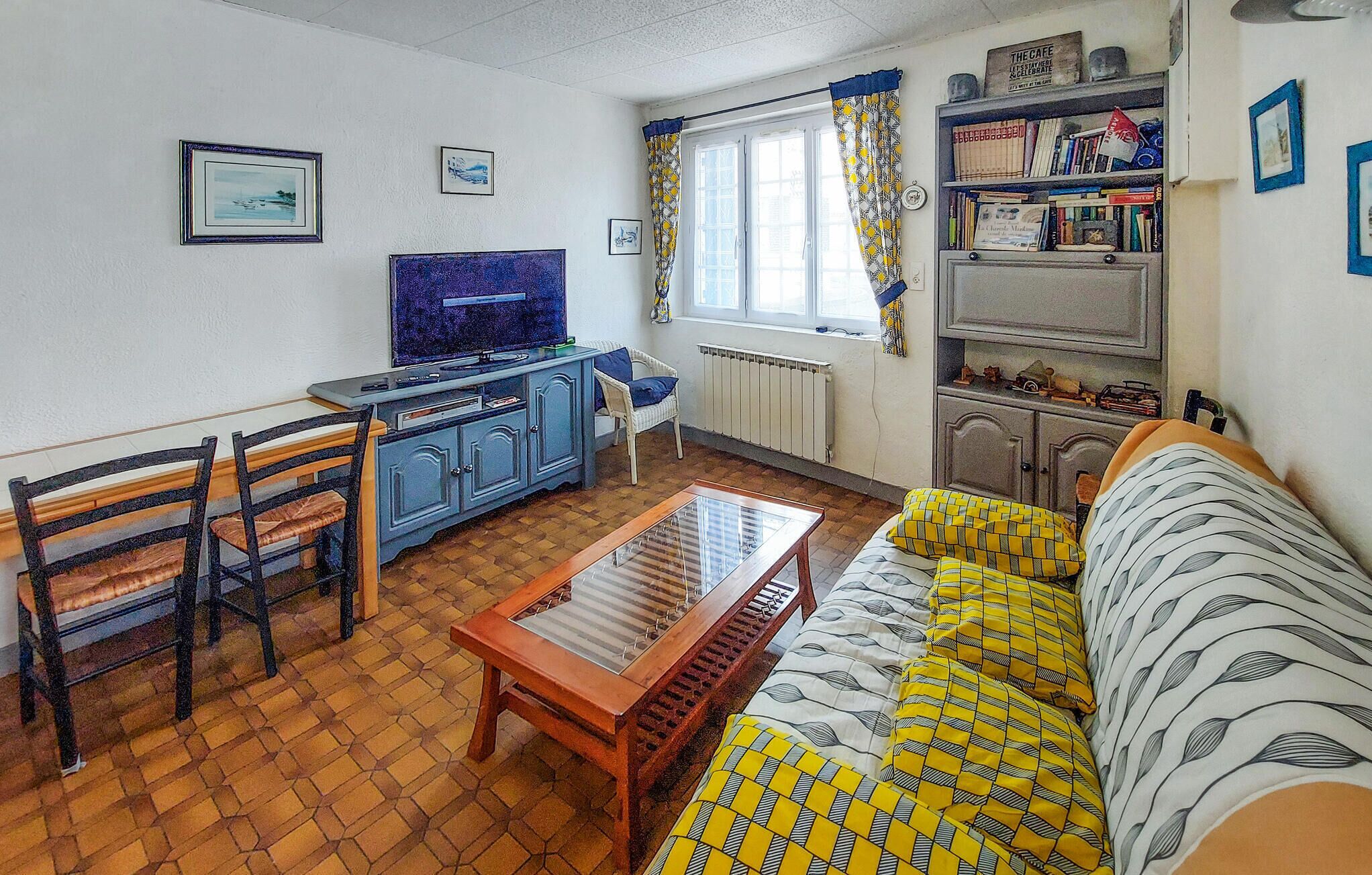 A living room with a sofa, a wooden coffee table, a TV, a bookshelf, and a window with curtains.
