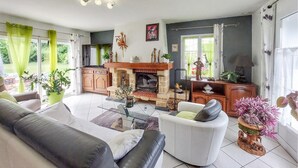 A living room with a fireplace, sofa, armchair, and potted plants.