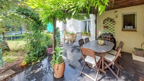 An outdoor patio with a round table and chairs, surrounded by potted plants and a pergola.