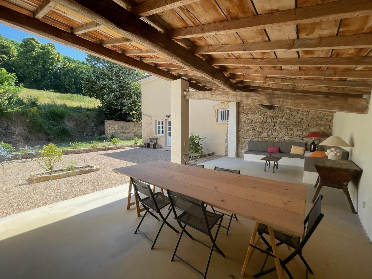 Een terras buiten met een houten tafel en stoelen, een stenen muur en een stenen bank.
