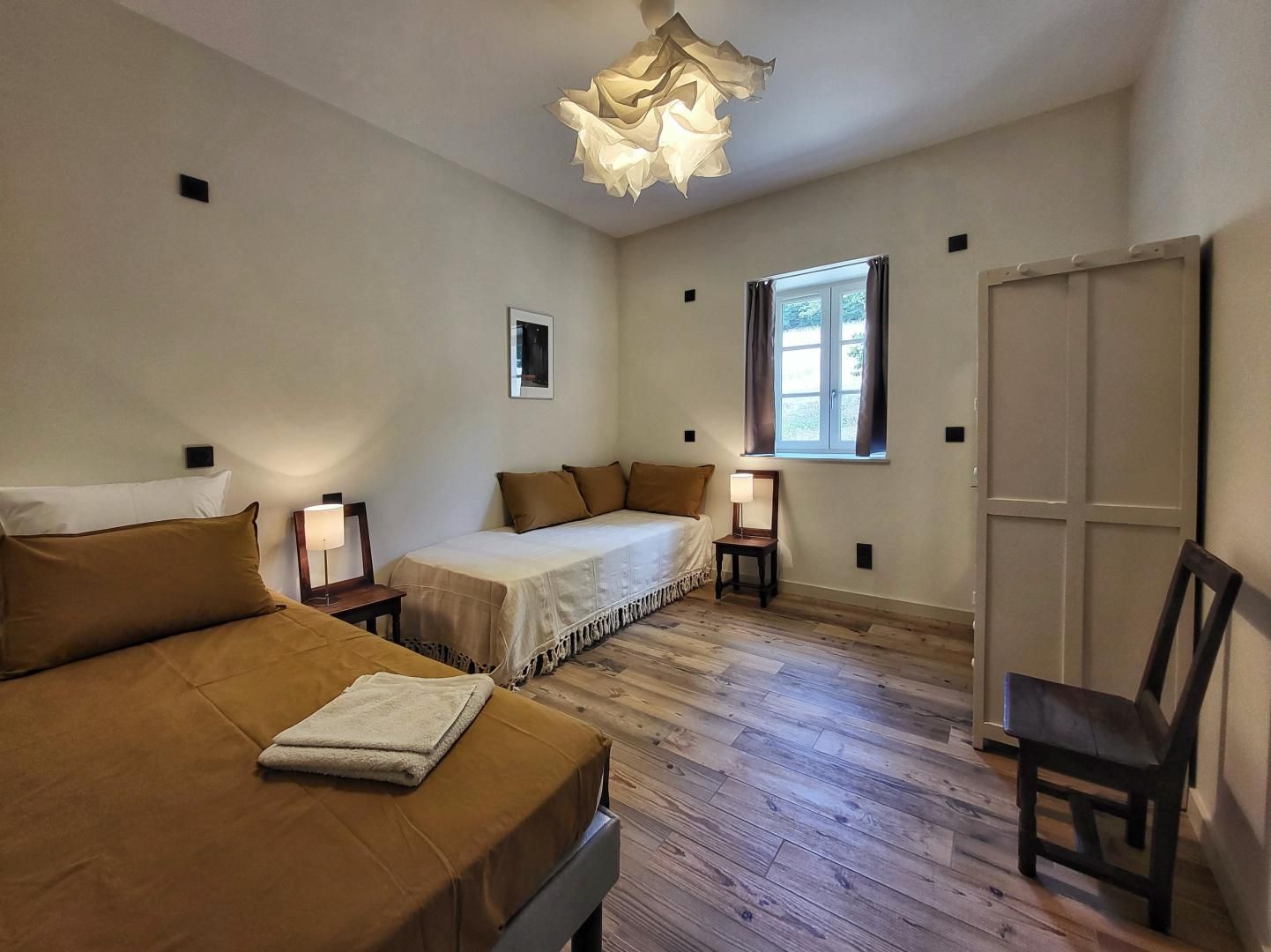 Quarto com cama, cadeira, mesa de cabeceira, abajur, janela e porta.