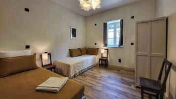Quarto com cama, cadeira, mesa de cabeceira, abajur, janela e porta.