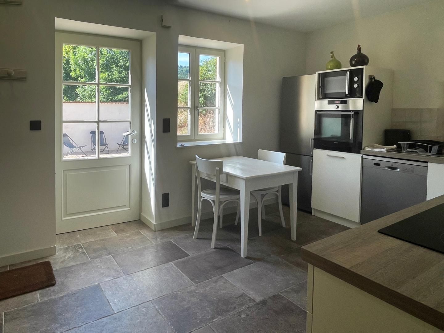 Une cuisine moderne avec une table et des chaises blanches, un four encastré, un four à micro-ondes et un lave-vaisselle.