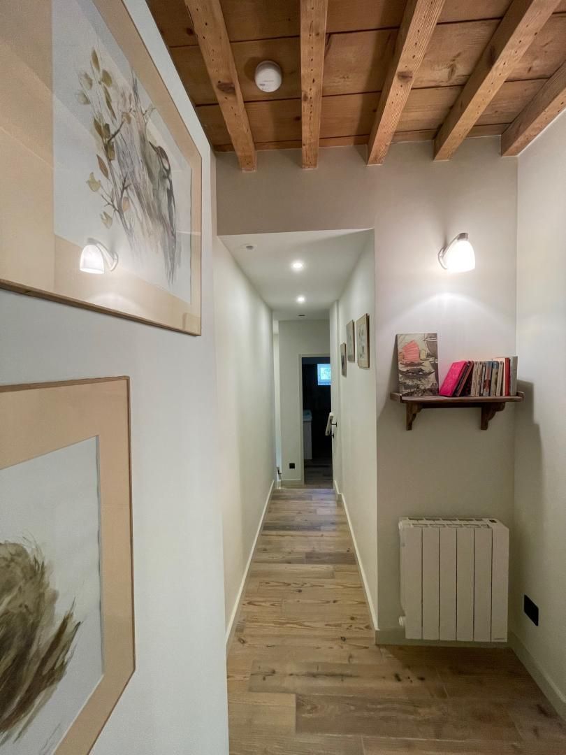 Un couloir avec des poutres en bois, des œuvres d’art encadrées, un radiateur et une étagère remplie de livres.