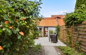 A garden with a wooden fence, a pathway leading to a building with a tiled roof, and a table with chairs outside. - 1 bedroom lovely home in Assens (Assens)