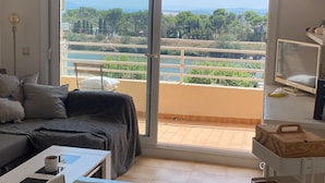A room with a sliding glass door leading to a balcony with a view of greenery and a distant landscape. - Well-equipped apt, in the center of town, near beach and shops, overlooking natural park and sea. (Empuriabrava)
