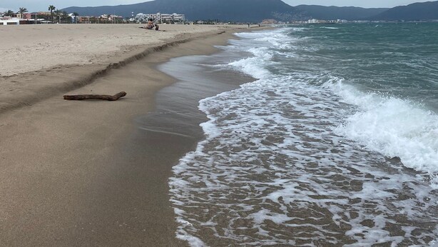 A beach with a sandy shore, waves, and distant mountains under a cloudy sky. - Well-equipped apt, in the center of town, near beach and shops, overlooking natural park and sea. (Empuriabrava)
