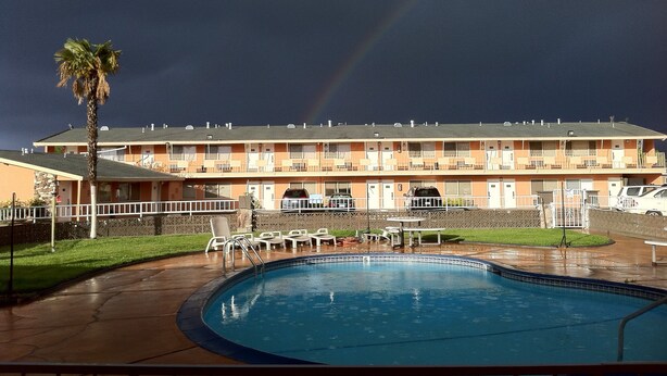 Un motel avec une piscine, un palmier et un arc-en-ciel dans le ciel.