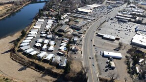 Vue aérienne d’une zone commerciale comprenant plusieurs entrepôts, un parking et un pont enjambant une rivière.