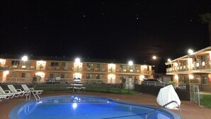 Une piscine avec des chaises longues, une table et un espace abrité.