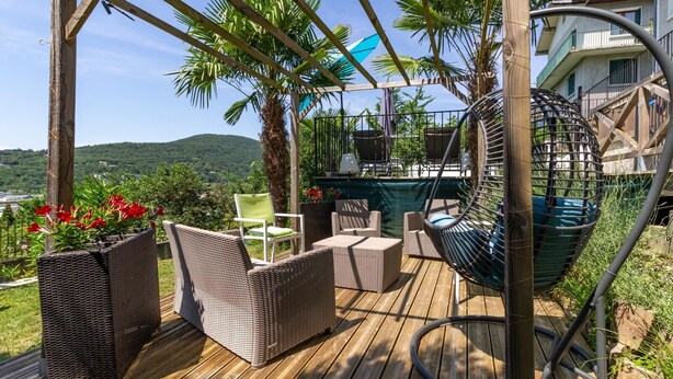 Eine Holzterrasse mit Korbmöbeln, einem Hängesessel und einem Poolbereich mit Bergblick.