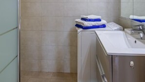Ein Badezimmer mit Duschkabine aus Glas, einem Waschbecken inklusive Spiegel und einem Handtuchhalter mit gefalteten Handtüchern.