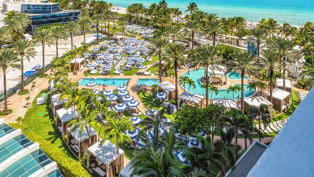 Un resort con varias piscinas, palmeras y vista al océano.