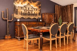 Ein Essbereich mit einem Holztisch, sechs Stühlen, einem Kaktus, einem Gemälde eines historischen Gebäudes und einem Holzschrank.