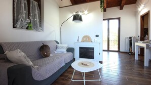 Un salón con un sofá gris, una mesita auxiliar blanca, una lámpara de pie y un ventanal corredero que da a un espacio exterior.