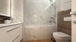 A modern bathroom with a marble shower, a toilet, and a vanity with drawers.