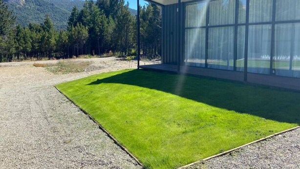 A modern building with a glass facade, a well-maintained lawn, and a mountainous backdrop.