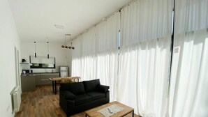 A modern living room with a black sofa, a wooden coffee table, and a kitchen in the background.