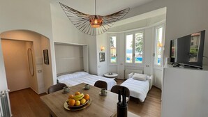 A modern hotel room with two beds, a dining table with fruit, a TV, and large windows. - Stresa Golf & Relax Romantik Suite (Gignese)