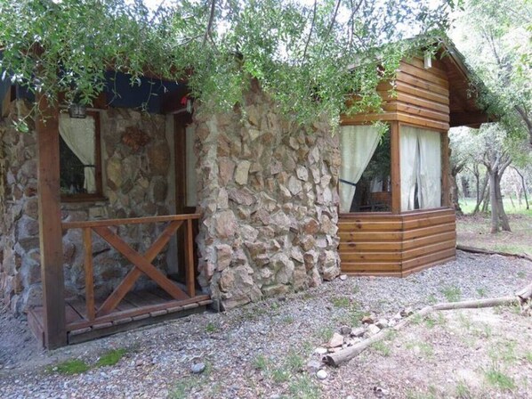 Una cabaña rústica de piedra con vigas de madera, que cuenta con un porche y un ventanal pequeño.