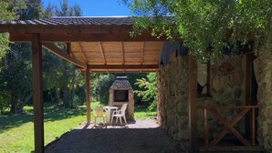 Un patio al aire libre con pared de piedra, pérgola de madera y una parrilla.