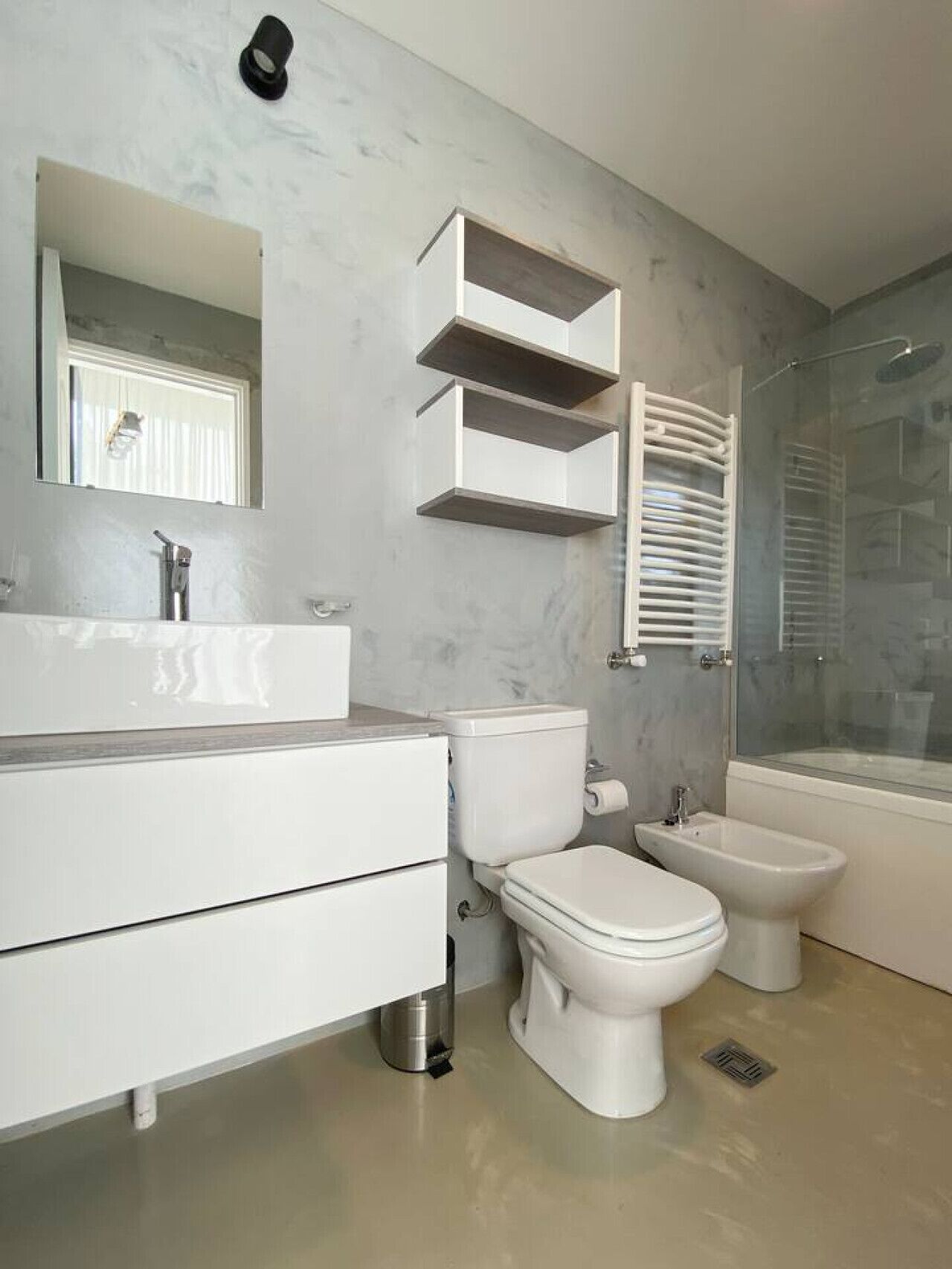 Casa de banho moderna com toucador branco, sanita, bidé e cabine de duche em vidro.