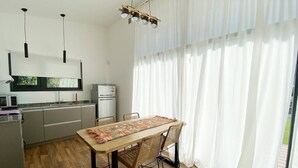 A modern kitchen with a dining area, featuring a wooden table, wicker chairs, and a view through large windows.