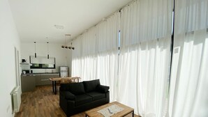 A modern living room with a black sofa, a wooden coffee table, and a kitchen area in the background.