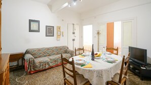 A dining area with a round table set for four, a sofa, and a television.