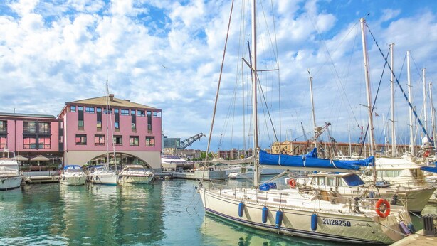 A marina with multiple boats docked, a pink building, and clear skies.